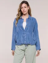 Camperita de denim liviano color azul, con cuello camisero, botones frontales ocultos, mangas largas de hombros caídos, bolsillos laterales y cordón ajustable en la cintura.
