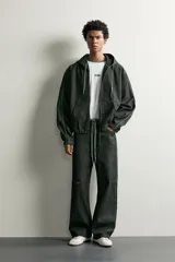 Cazadora de denim color negro con capucha ajustable con cordones, cierre frontal de cremallera, bolsillos tipo canguro y detalles de costuras en contraste en las mangas.