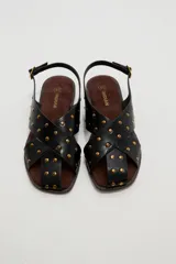 Sandalias planas de cuero sintético marrón, con tiras cruzadas en el empeine y tachas metálicas doradas distribuidas por toda la capellada. Cuenta con tira ajustable en el talón con hebilla.