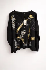 Buzo de tejido de punto abierto color beige, con diseño holgado, cuello redondo y mangas largas con puños acanalados. Presenta un estampado artístico que combina motivos de animal print y detalles brillantes en color dorado.