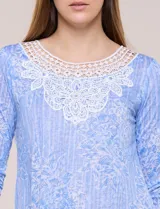 Blusa celeste con estampado floral devoré, de manga tres cuartos, escote redondo amplio y detalle de pechera de encaje blanco en contraste.