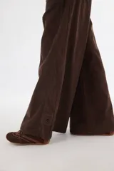 Pantalón sastrero de tiro medio confeccionado en pana de algodón. Presenta un diseño de pierna ancha con costuras verticales decorativas, bolsillos delanteros y traseros, y un detalle de aplique con ojalillo metálico en el ruedo de una de las piernas.