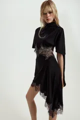 Vestido midi de terciopelo negro con cuello redondo y pañuelo integrado en el mismo tejido. Presenta mangas cortas, aberturas laterales con detalle de encaje a tono y bajo asimétrico con terminación en encaje.