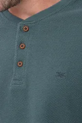 Remera de algodón texturada color gris oscuro, de manga larga, con cuello redondo y botones en la parte frontal. Presenta un pequeño logo bordado en el pecho y un parche decorativo en la manga izquierda.