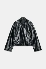 Chaqueta de Zara Woman Collection en tejido con acabado brillante efecto cuero. Presenta cuello solapa, manga larga con trabillas ajustables, bolsillos delanteros y cierre frontal con botones ocultos bajo solapa.