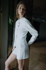 Chaqueta de punto de cuello redondo y manga larga, en color blanco, con cierre frontal asimétrico de botones negros.