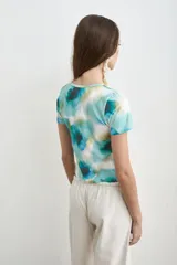 Remera de manga corta con estampado estilo acuarela en tonos de turquesa, verde y blanco, de cuello redondo y corte ajustado.