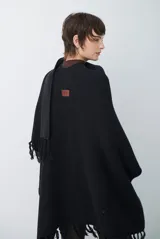 Ruana de tejido de punto en color negro, con diseño de cuello alto y terminaciones con flecos en los bordes.