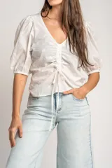 Blusa marrón de algodón con bordados sutiles, escote en V, mangas cortas abullonadas y detalle de fruncido con cordón ajustable en el centro del frente.