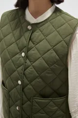 Chaleco acolchado de color negro con diseño de rombos, cierre frontal con botones metálicos a presión y dos bolsillos delanteros aplicados.