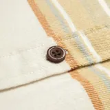 Camisa de franela a rayas horizontales en tonos beige, marrón y blanco, con cuello clásico, cierre frontal con botones y dos bolsillos con solapa en el pecho.