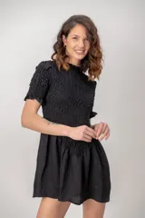 Vestido corto de color negro, con cuerpo y mangas cortas de nido de abeja fruncido, y falda corta con vuelo.