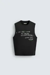 Camiseta sin mangas (tank top) negra, corte boxy fit, con cuello redondo y sisa con acabado irregular. Presenta un estampado frontal con texto manuscrito en verde y blanco que dice: "I look cool online, but offline I'm even better... Chase real likes!".