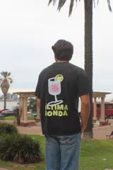 Remera negra de algodón peinado, de corte recto y mangas cortas. En la espalda presenta una estampa intervenida a mano que ilustra una copa de trago y la leyenda "Última Ronda" en color amarillo.