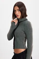 Campera corta de tejido de punto acanalado con diseño de rayas verticales en dos tonos. Presenta cuello alto y cierre frontal completo con borde en color negro.