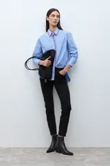 Camisa de corte clásico con estampado de rayas verticales en tonos celestes y blancos. Presenta un detalle de bordado decorativo en color rojo a lo largo de la botonadura frontal y el cuello, mangas largas con puños abotonados y un bolsillo frontal en el pecho.