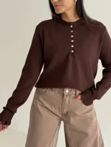 Sweater de punto color marrón chocolate, con cuello redondo y cierre frontal parcial con botones. Presenta mangas largas con puños acampanados y detalle de volados.