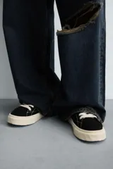 Zapatillas bajas de lona negra con cordones blancos y suela de goma blanca con textura.