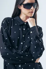 Camisa de corte clásico con estampa de lunares blancos sobre fondo negro, manga larga con puños abotonados y bolsillo frontal.