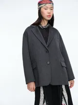 Chaqueta de paño color gris oscuro, de corte amplio y estructura holgada. Presenta solapas clásicas, cierre frontal con dos botones y bolsillos laterales con solapa.