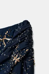 Falda corta de tiro medio confeccionada en tejido tipo tul color azul marino. Presenta un diseño con drapeado lateral en la cintura, bordados florales con aplicación de abalorios y bajo asimétrico.