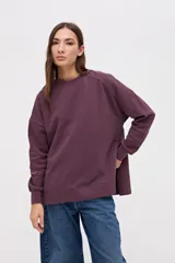 Buzo oversize de felpa con friza, color bordó, con cuello redondo, mangas largas con cortes decorativos y tajos laterales en el ruedo. Presenta un bordado de la marca en una de las mangas.