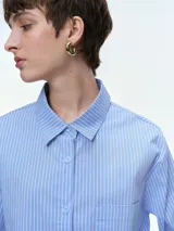 Camisa oversize de popelina de algodón con diseño de rayas verticales, cuello clásico, cierre frontal con botones, manga larga con puños anchos y bolsillo aplicado en el pecho.