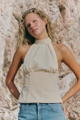 Top halter combinado con cuello subido ajustable mediante botones y hombros descubiertos, de diseño bicolor en tonos beige y blanco con sutiles rayas verticales.