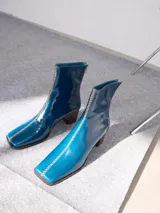 Botas de cuero color marrón con caña media y punta cuadrada. Presentan un cierre trasero, tirador para calzar fácilmente y bordado en color contrastante en el empeine. Suela de goma y taco de madera de 6 cm de altura.