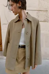 Chaqueta de corte recto y estilo camisero en color beige, con cuello solapa, manga larga y cierre frontal con botones. Presenta dos bolsillos delanteros de plastrón.