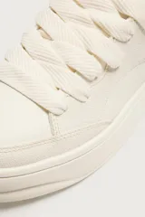 Zapatilla deportiva de diseño monocolor en tono crema, con cordones al tono y suela de plataforma con volumen.