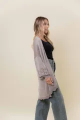 Cardigan tejido liviano color beige con efecto brillante y calados en las mangas. Diseño abierto y corte relajado.