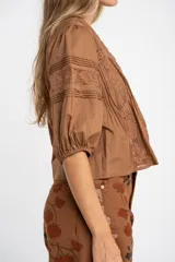 Blusa de algodón color marrón con cuello en V, mangas tres cuartos con puños elásticos y detalles de encaje y alforzas en el frente.