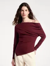 Blusa negra de manga larga con diseño asimétrico en el escote, dejando un hombro al descubierto. Presenta un corte ajustado con detalle de frunces laterales que crean un efecto drapeado en el torso.