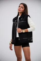 Chaleco negro de estilo aviador con interior y bordes de corderito sintético. Presenta cierre frontal metálico, detalles de tiras de cuero sintético y hebillas ajustables en el cuello y el ruedo.