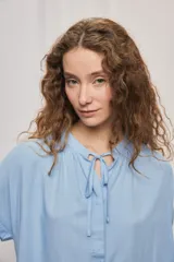 Camisa de manga corta color celeste, confeccionada en viscosa fluida, con silueta amplia y escote redondo con frunces y lazo para anudar.