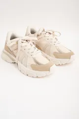 Zapatilla deportiva de diseño urbano en tonos neutros, combinando paneles de malla, gamuza y detalles metalizados en color dorado. Cuenta con suela robusta y acordonado frontal.