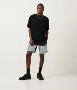 Bermuda deportiva de tejido plano de poliamida, color negro y gris claro, con bloques de color reflectivo en la parte inferior. Presenta cintura elástica con amarre y un pequeño logo de la NASA en la pierna derecha.