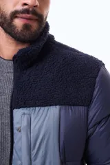 Campera puffer negra con paneles de textura tipo corderito en la parte superior del pecho y hombros. Cuenta con cierre frontal, puños y ruedo acanalados, y un bolsillo vertical con cierre en el pecho.