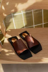 Sandalias planas con punta cuadrada, base negra y capellada de cuero marrón con textura trenzada.