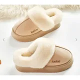 Pantuflas de gamuza color beige con plataforma y forro interior de corderito sintético. Presentan un diseño sin talón con el nombre de la marca bordado en el lateral.