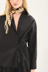 Camisa de popelina de algodón en color negro, con corte amplio, cuello clásico y cierre frontal con botones. Presenta un diseño versátil con botones en los laterales que permiten un ajuste cruzado.