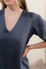 Vestido largo azul oscuro de lino 100% con escote en V, mangas abullonadas con elástico en el puño y pespunte en contraste. Presenta detalle de punto smock en el canesú y bolsillos laterales.
