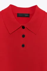 Jersey de punto blanco con rayas horizontales negras, cuello polo blanco y manga corta. Presenta una botonera frontal de tres botones negros.