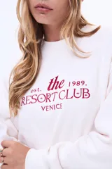 Buzo de felpa color blanco con cuello redondo y estampa frontal en color bordó con la leyenda 'the resort club venice'.