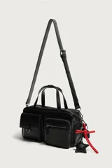 Bolso bandolera negro de acabado liso, con compartimento principal con cierre de cremallera. Cuenta con dos bolsillos frontales, uno con solapa y detalle metálico y otro con cremallera. Incluye dos asas de mano y un asa de hombro ajustable y extraíble, además de detalles de charms y mosquetón en un lateral.
