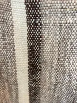 Poncho de lana virgen tejido en telar con diseño geométrico a rayas en tonos gris, marrón y celeste, con apliques de cuero en el escote y flecos en el ruedo.