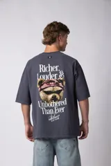 Remera de corte oversize color gris oscuro, confeccionada en algodón premium de alto gramaje. Presenta un diseño minimalista con un pequeño estampado frontal que incluye un oso y el texto 'Richer & Louder VCP'.
