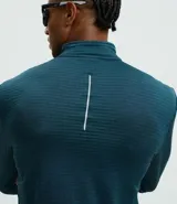 Remera deportiva de manga larga con cuello alto y cierre frontal parcial. Presenta una textura acanalada en toda la prenda y detalles reflectivos en los hombros.