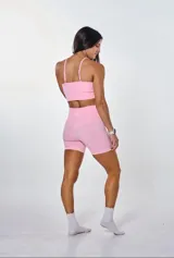 Conjunto deportivo de dos piezas color rosa, compuesto por un top de tirantes finos con logo estampado en el frente y un short de tiro alto con diseño sin costuras.